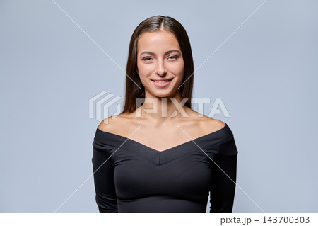 Portrait of confident young woman in off-shoulder black top against grey background Portrait of confident young woman in off-shoulder black top against grey background 143700303