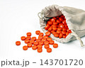 Bright orange round tablets scattered and spilling out of an opened gray suede drawstring pouch on a clean white background, conceptual photo about not knowing what is inside until the bag is opened 143701720