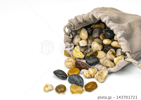 Close-up of a beige suede drawstring bag tipped over with assorted polished river stones in white, yellow, brown and black tumbling out, conceptual image of mystery, hidden value, risk and surprise 143701721