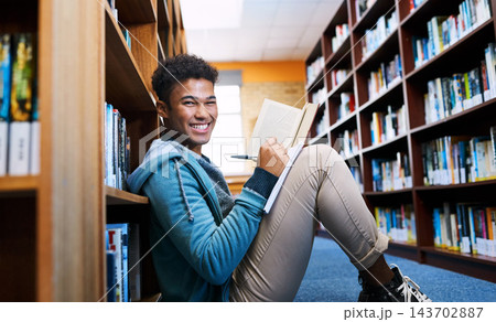Student, man and portrait with studying in library for scholarship, writing and reading a book for exam information. Education, person or happy with notebook for research notes and knowledge on floor Student, man and portrait with studying in library for scholarship, writing and reading a book for exam information. Education, person or happy with notebook for research notes and knowledge on floor 143702887