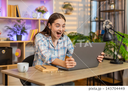 Young woman on home table smiling at laptop celebrating success with applause indoors in living room 143704449