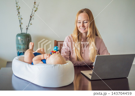 Baby discovering a colorful rattle with mother beside her home computer. Baby discovering a colorful rattle with mother beside her home computer. 143704459