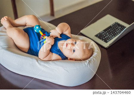 Curious infant exploring a rattle beside computer equipment in a home workspace. Curious infant exploring a rattle beside computer equipment in a home workspace. 143704460
