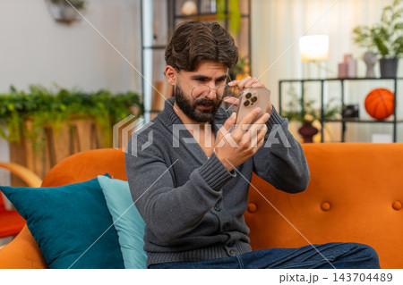 Indian man with eyeglasses squints at smartphone screen tries to read small text poor vision focus Indian man with eyeglasses squints at smartphone screen tries to read small text poor vision focus 143704489