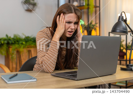 Young woman works on laptop sees game loss failed bet and grim news sighs feels upset disappointed 143704490
