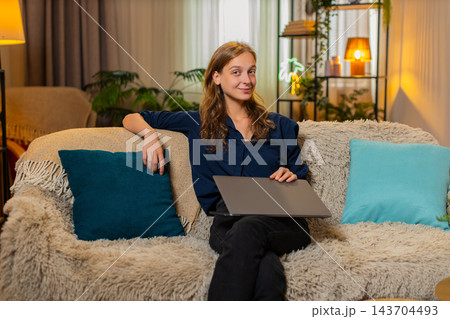 Young woman on home sofa closes laptop after work leans back exhales deeply and smiles with relief 143704493