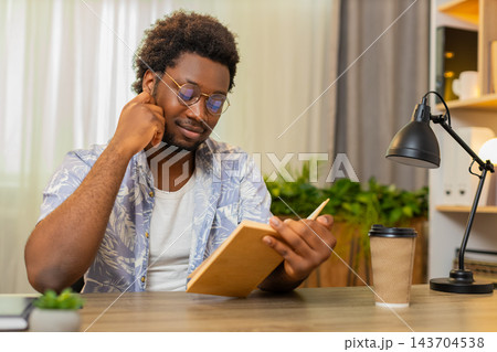 African American young man on home table reads book with focus and learns new ideas for self growth African American young man on home table reads book with focus and learns new ideas for self growth 143704538