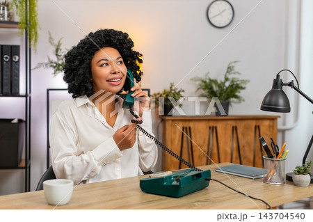 African American businesswoman laughs talking on retro old phone smiling kindly during client call 143704540
