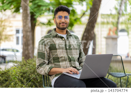 Indian man working on laptop in city street park smiling during remote online freelance job outdoors Indian man working on laptop in city street park smiling during remote online freelance job outdoors 143704774