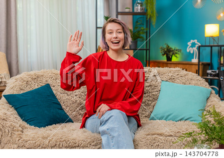 Young woman happily waving hand hello gesture friendly cheerful greeting expression smiling joyfully 143704778