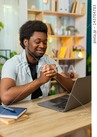 African American young man on home table rubbing hands during laptop work pause for web job indoors African American young man on home table rubbing hands during laptop work pause for web job indoors 143704783