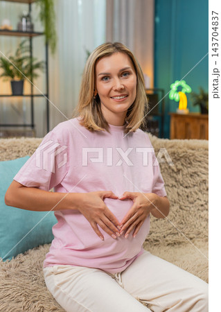 Pregnant woman forming heart with hands over belly smiling enjoying sweet loving moment before birth 143704837