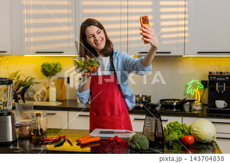 Young woman showing fresh salad on smartphone video call in home kitchen for healthy diet lifestyle 143704838