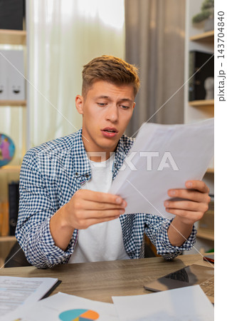 Young man on home table checking client payments and reviewing unpaid bill with worried expression Young man on home table checking client payments and reviewing unpaid bill with worried expression 143704840
