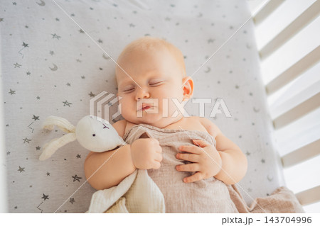Baby sleeping in a crib with a soft rabbit comforter and blanket. 143704996