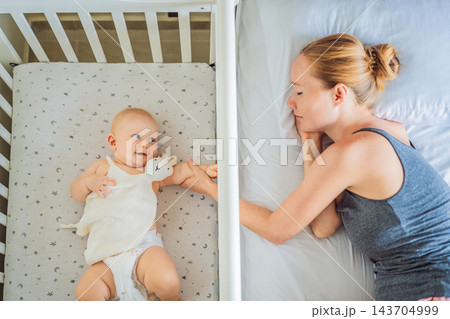 Woman tending to her infant while resting beside the baby's crib. Woman tending to her infant while resting beside the baby's crib. 143704999