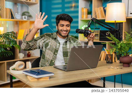Indian man on home table recording video blog with microphone and laptop sharing advice with smile Indian man on home table recording video blog with microphone and laptop sharing advice with smile 143705040