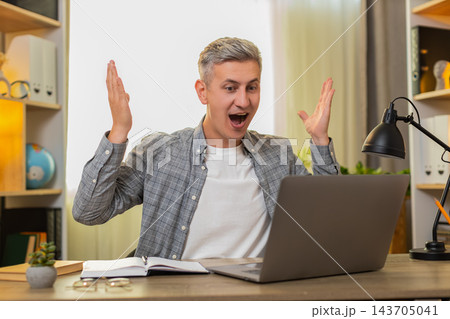 Middle-aged man on home table celebrates job invitation email and online game win on laptop with joy 143705041