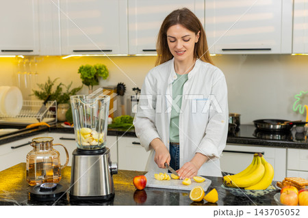 Middle-aged woman cutting apple for smoothie with blender in kitchen for healthy breakfast diet plan 143705052