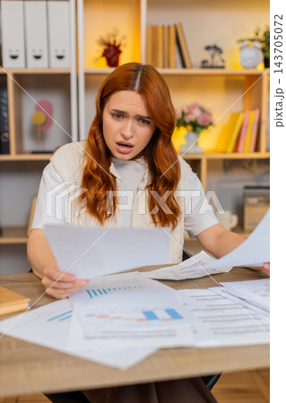 Young woman on home table sorting papers and feeling stressed by confusing household paperwork mess Young woman on home table sorting papers and feeling stressed by confusing household paperwork mess 143705072