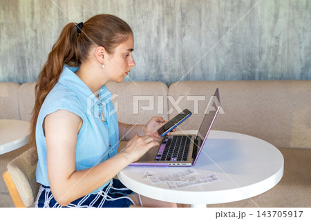 Young woman working on laptop and phone at cafe table while focusing on online tasks 143705917