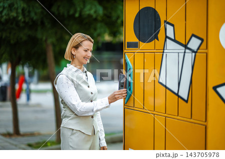 Woman using smartphone for parcel pickup at automated locker 143705978
