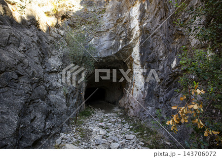 Entrance to a dark rocky cave and underground tunnel in a rugged 143706072
