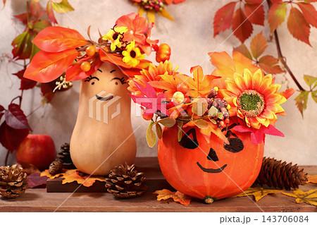 Pumpkins adorned with festive leaf wreaths and playful faces with googly eyes, along with apples and rowan berries, all set on an old wooden table, Thanksgiving theme, rustic harvest, banner 143706084