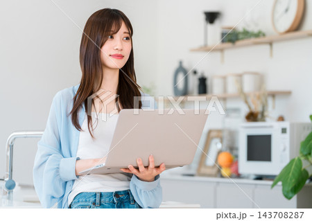 おしゃれな家のキッチンでノートパソコンを持ち考える若い女性 143708287