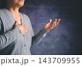A cropped person in a gray knit cardigan rests one hand on the chest and extends the other with an open palm against a dark blue background, leaving copy space for a message about openness. 143709955