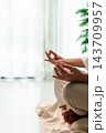 Close view of a person sitting cross-legged with hands on the knees in a meditation-style gesture near a bright window, leaving generous vertical copy space for mindfulness or relaxation content. 143709957