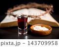 Dark red beverage and communion wafers before an open book with a thorn wreath, creating a reflective Christian still life for scripture study, worship, prayer, sacrifice, faith, and remembrance. 143709958