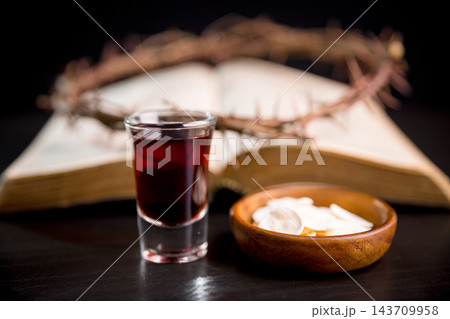 Dark red beverage and communion wafers before an open book with a thorn wreath, creating a reflective Christian still life for scripture study, worship, prayer, sacrifice, faith, and remembrance. Dark red beverage and communion wafers before an open book with a thorn wreath, creating a reflective Christian still life for scripture study, worship, prayer, sacrifice, faith, and remembrance. 143709958