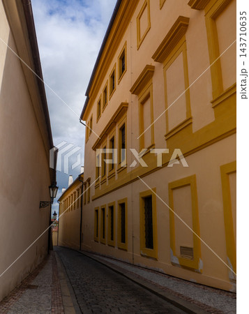 A narrow cobblestone alley in Prague features a tall, historic yellow building A narrow cobblestone alley in Prague features a tall, historic yellow building 143710635