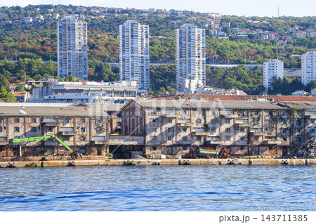 he image shows a waterfront with old, weathered industrial buildings in the foreground and modern high-rise apartment buildings in Rijeka, Croatia he image shows a waterfront with old, weathered industrial buildings in the foreground and modern high-rise apartment buildings in Rijeka, Croatia 143711385