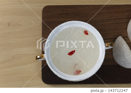 Top view of cooked edible bird nest soup with goji berries in a white bowl next to a raw dry bird nest cup on a wooden board Top view of cooked edible bird nest soup with goji berries in a white bowl next to a raw dry bird nest cup on a wooden board 143712247