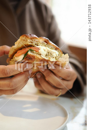 Person holding a sandwich with tomato and cheese at a cafe table 143712938