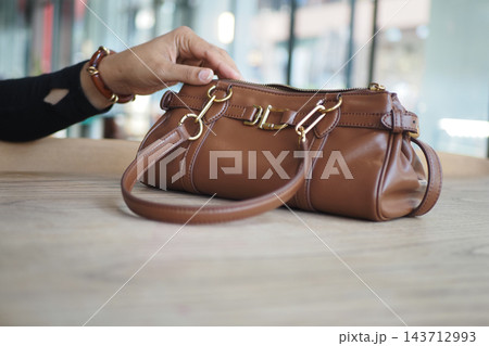 Hand lifting a brown leather handbag from a table in a shop Hand lifting a brown leather handbag from a table in a shop 143712993