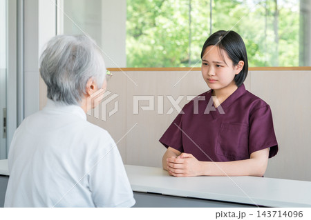 介護施設の相談窓口でシニア女性の相談に対応する若い女性介護スタッフ 143714096