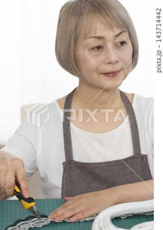 リビングで趣味のDIYでドールチェアーをリメイクするシニア女性 143714442