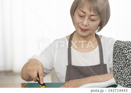 リビングで趣味のDIYでドールチェアーをリメイクするシニア女性 143714443