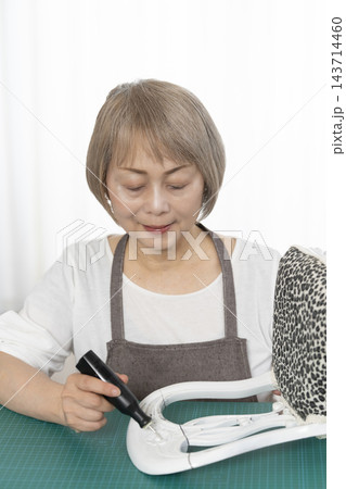リビングで趣味のDIYでドールチェアーをリメイクするシニア女性 143714460