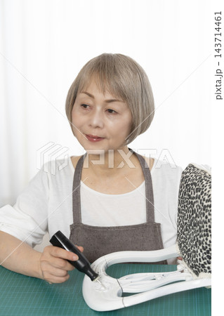 リビングで趣味のDIYでドールチェアーをリメイクするシニア女性 143714461