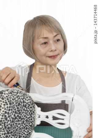 リビングで趣味のDIYでドールチェアーをリメイクするシニア女性 143714468