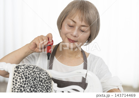 リビングで趣味のDIYでドールチェアーをリメイクするシニア女性 リビングで趣味のDIYでドールチェアーをリメイクするシニア女性 143714469