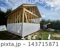 Nonwoven polypropylene fabric covers lower timber wall framing as wind barrier on unfinished frame house, with two workers handling building materials nearby. 143715871