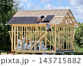 Roofing installation with corrugated bitumen sheets on pitched roof of timber frame building under construction with exposed wall studs. 143715882