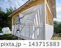 Wind and water resistant membrane made from nonwoven polypropylene fabric is spread across wooden wall frame by worker for moisture protection. 143715883