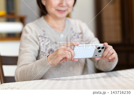 家のリビングでスマホで動画を見るミドル・シニア女性 家のリビングでスマホで動画を見るミドル・シニア女性 143716230