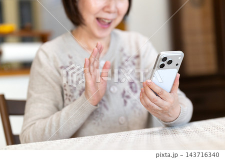 家のリビングでスマホを見て喜ぶミドル・シニア女性 143716340